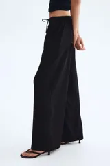 Pantalón negro de tiro alto, confeccionado en tejido texturizado con corte holgado y piernas amplias. Cuenta con cintura elástica fruncida y cordón ajustable.