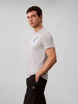 Remera gris melange de manga corta con cuello redondo, confeccionada en algodón regenerativo. Cuenta con un pequeño estampado gráfico del monograma y la inscripción de la marca en el pecho.