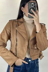 Chaqueta corta tipo biker confeccionada en gamuza color beige, con cierre frontal cruzado, solapas amplias, bolsillos con cierre y cinturón ajustable en la cintura.
