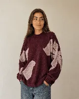 Buzo tejido de algodón y acrílico color bordó, de silueta amplia y relajada, con cuello alto y diseño floral en tonos rosados. Cuenta con terminaciones acanaladas en cuello, puños y ruedo.