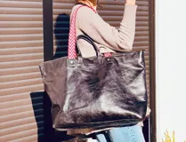 Bolso XL de cuero color marrón oscuro, con asas cortas de cuero y correa larga de tela estampada a rayas rojas y blancas.