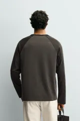 Camiseta de corte regular con cuello redondo y mangas largas tipo raglán en contraste. Presenta un diseño bicolor con efecto lavado.