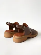 Sandalias de cuero color chocolate con suela track y taco bajo cuadrado. Poseen capellada cerrada con aberturas laterales y tira ajustable en el talón con hebilla metálica.
