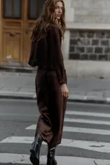 Chaqueta de cuello solapa y manga larga, color marrón oscuro, con efecto ante. Presenta bolsillos delanteros de plastrón, cierre frontal con botones y un bajo troquelado con diseño floral y acabado festoneado.