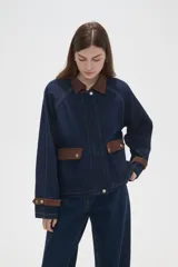 Campera de jean azul oscuro con cuello y puños de pana en color marrón. Presenta cierre frontal, costuras a la vista y detalles de botones metálicos en los puños.