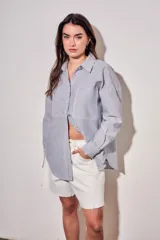Camisa de corte oversize con diseño de rayas verticales en tonos azul y blanco. Presenta cuello clásico, cierre frontal con botones y mangas largas con puños abotonados.
