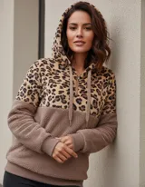 Buzo tipo canguro con capucha, confeccionado en tejido polar. Presenta un diseño combinado con estampado animal print en la parte superior y color marrón liso en la parte inferior. Incluye cierre frontal parcial, cordones ajustables en la capucha y puños de tejido acanalado.