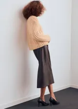 Cardigan de punto grueso color beige, de cuello redondo, manga larga y diseño recto. Presenta cierre frontal con botones efecto joya.