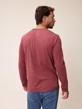 Remera de manga larga con cuello redondo y cierre frontal parcial con botones. Presenta un diseño de color sólido con un pequeño logo bordado en el pecho.