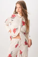 Pijama de satén compuesto por una camisa de manga larga con botones y un pantalón largo, ambos de color crudo con estampado de rayas verticales negras y flores rojas.