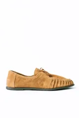 Mocasín de estilo relajado confeccionado en cuero gamuzado color tostado. Presenta detalles fruncidos en la puntera, cordones decorativos en el empeine y el logo de la marca grabado en el lateral.
