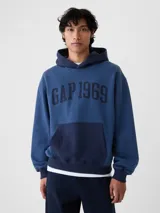 Buzo tipo canguro con capucha, de color azul con bolsillo frontal tipo canguro en un tono azul más oscuro. Presenta el logo 'GAP 1969' estampado en el pecho en color azul marino.