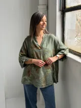 Blusa verde de lino con estampado de flores grandes en tonos marrones y verde oliva, con cuello en V y un botón decorativo central.