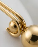 Caravanas colgantes de acero con baño de oro, compuestas por un gancho alargado y una esfera metálica lisa en el extremo inferior.