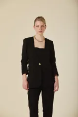 Saco de mujer con diseño estructurado, cuello redondo sin solapas, cierre frontal con un botón metálico dorado y mangas tres cuartos con detalle de frunces. Presenta bolsillos laterales con solapa.
