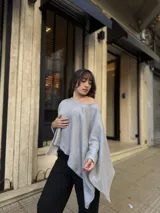 Poncho de hilo liviano en color gris, con diseño sin cuello y caída fluida. Presenta un corte asimétrico y una textura tejida, ideal para superponer sobre otras prendas.