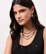 Conjunto de bijouterie compuesto por un collar multicapa de hilo encerado negro con separadores metálicos texturizados y un par de aros cuadrados con superficie texturizada.