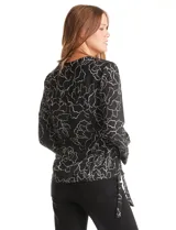 Blusa de gasa estampada con flores blancas sobre fondo negro, marca Zac & Rachel. Presenta cuello a la base, escote en V con abertura de botones y mangas 3/4 amplias. Los laterales tienen lazo.