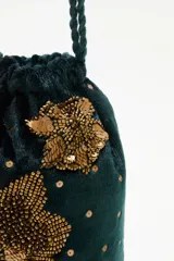 Cartera tipo bolso de mano color negro, confeccionada en terciopelo con bordados de estrellas y aplicaciones de pedrería brillante. Cuenta con correas trenzadas de cordón negro y cierre superior.