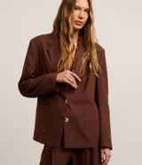 Blazer oversized de Marfinno color marrón, confeccionado en mezcla de viscosa, poliéster y lino. Presenta solapas clásicas en el cuello, cierre frontal abotonado y bolsillos delanteros.