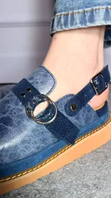 Zuecos cerrados tipo sandalias de plataforma, confeccionados en cuero con efecto craquelado en tono azul, con tiras texturizadas, argollas metálicas decorativas y tira trasera con hebilla regulable.