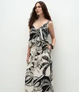 Pollera larga (midi) de corte evasé, con cintura elástica y lazo. Presenta un estampado grande en blanco y negro de motivos tropicales como hojas de palmera y flores.