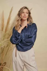 Blusa de satén color azul marino, con cuello mao, cierre frontal de botones y mangas largas con puños elásticos. Presenta detalles fruncidos en los hombros.