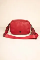 Cartera tipo bandolera de diseño trenzado, con correa ajustable y desmontable, y detalle de borlas laterales.