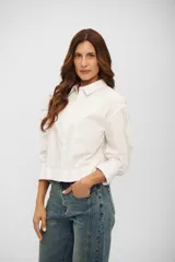 Camisa de corte cropped y diseño holgado, color blanco, con cuello clásico, cierre frontal de botones y mangas largas con puños anchos.