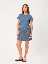 Falda corta de corte suelto, confeccionada en algodón con diseño de rayas verticales azules y blancas, bolsillos laterales y cierre frontal con botón y cremallera.