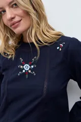 Blusa blanca de manga larga con cuello redondo, confeccionada en tela liviana con detalles de encaje vertical y bordado floral en el pecho.