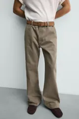 Pantalón de denim color verde oliva, estilo chino con corte ancho y bota acampanada (flare) desde la rodilla. Tiro medio, confeccionado en tejido rígido. Presenta bolsillos frontales y bolsillos traseros de plastrón.