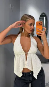 Top halter de tejido de punto color blanco, con escote en V pronunciado, diseño abierto en el frente y bajo asimétrico en punta.