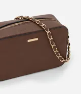 Cartera bandolera pequeña de textura granulada, con cierre superior de cremallera y correa de cadena entrelazada con material sintético. Presenta un diseño rectangular con placa metálica decorativa en el frente.