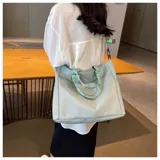 Bolso tipo tote color gris claro, con doble asa de mano y correa larga regulable. Tiene dos bolsillos laterales y un bolsillo frontal.