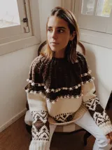 Sweater artesanal tejido a mano en lana merino, con diseño bicolor en marrón y tostado. Presenta un canesú texturado con trenzas y pequeños bodoques, cuello redondo y un patrón geométrico jacquard en mangas y cuerpo.