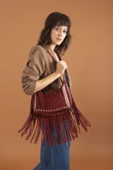 Bolso bandolera de gamuza color borgoña con flecos largos. Tiene correa de hombro con tachas plateadas y logo grabado en el frente.