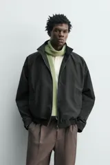 Cazadora bomber de corte relajado confeccionada en tejido técnico color negro. Presenta cuello subido, manga larga amplia, bolsillos de vivo en cadera, acabados elásticos y cierre frontal con cremallera de doble dirección.