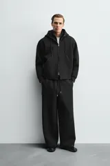 Pantalón de corte wide fit confeccionado en tejido técnico con efecto neopreno. Presenta cintura elástica ajustable con cordón, perneras anchas con costura frontal, bolsillos laterales y bolsillos traseros de plastrón.