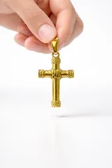 Dije en forma de cruz de acero color dorado, con detalles de textura trenzada en los extremos y en el centro.