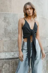 Top negro con breteles finos y escote en V. Presenta un nudo con aro metálico en la parte inferior del busto y un corte en el abdomen.