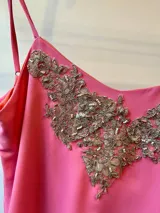 Vestido corto rosado con breteles finos, escote en V con aplique bordado dorado y volados en el ruedo.