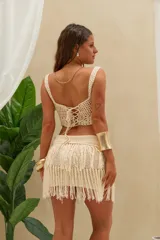 Conjunto de top y minifalda de crochet en color beige. El top es sin mangas con tirantes anchos y escote corazón, mientras que la minifalda cuenta con una pretina tejida y flecos largos colgantes.