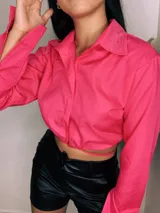 Camisa cropped negra con cuello clásico, mangas largas con puños abotonados y cierre frontal con botones. Presenta detalle de tachas plateadas en el cuello.