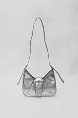 Cartera de hombro con acabado metalizado plateado, diseño estructurado con detalle de hebilla central decorativa y correas laterales ajustables.