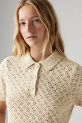 Remera color crema de tejido de punto calado, con cuello polo y mangas cortas.