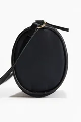 Cartera cilíndrica pequeña color negro con cierre superior y correa de hombro.