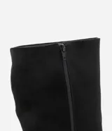 Bota de caña media con taco tipo anabela, confeccionada en gamuza sintética color negro. Presenta puntera fina, cierre lateral y diseño elegante con estructura ajustada.