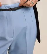 Pantalón carrot negro de sastrería, con bolsillos, pliegues y cinturón fino de cuero sintético.