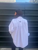 Camisa blanca de corte clásico con bordado de hilo negro en el hombro y bolsillo de cuerina negro en el pecho.